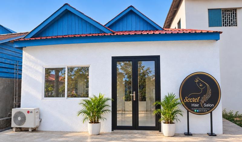The studio front: white walls, blue gables, a glass door between two palms and the round Secret Hair Salon sign