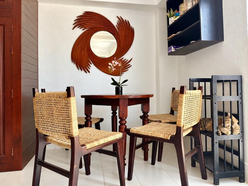 A round table and rattan chairs under a sunburst mirror